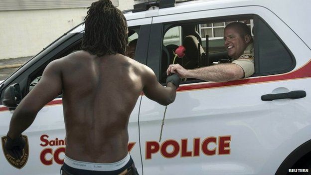 Resident John West (L) hands a rose to a police officer, showing his appreciation with help in cleanup efforts in Ferguson, Missouri, August 19