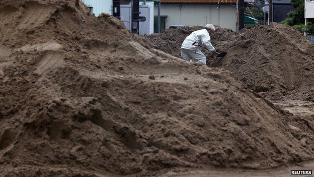 local resident removes mud in the rain at a site where a landslide swept through a residential area at Asaminami ward in Hiroshima, western Japan, August 22, 2014.