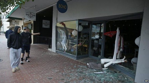 People walk past a fallen mannequin and broken storefront window in Napa