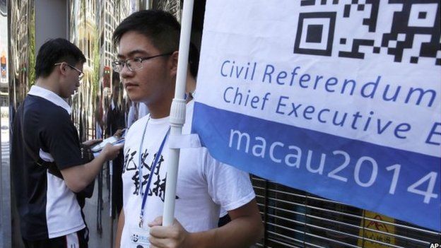 A man, left, votes on a tablet next to a volunteer with a banner promoting informal civil referendum in a street of the former Portuguese colony, Macau, Sunday, 24 Aug 2014.