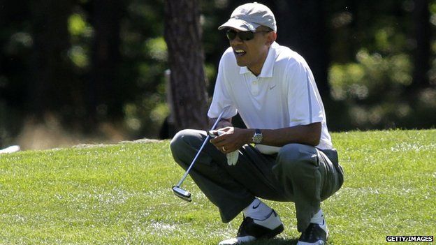 President Barack Obama squats by a golf course green.