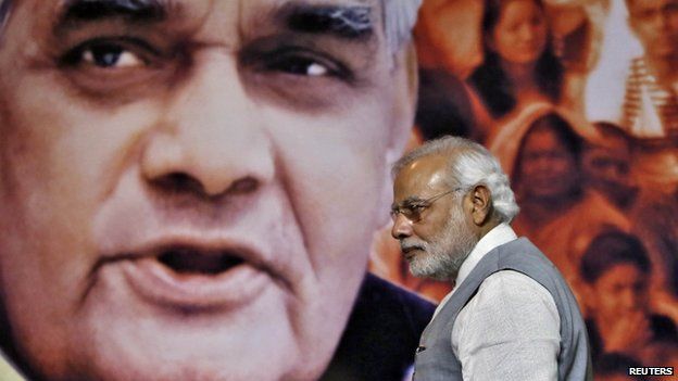 Indian Prime Minister Narendra Modi walks in front of a picture of former Indian Prime Minister Atal Behari Vajpayee after a news conference in New Delhi July 9, 2014.