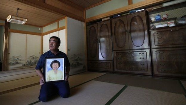 Mikio Watanabe holds a portrait of his late wife Hamako at his home at Yamakiya district in Kawamata town, Fukushima prefecture in this 23 June 2014 file photo