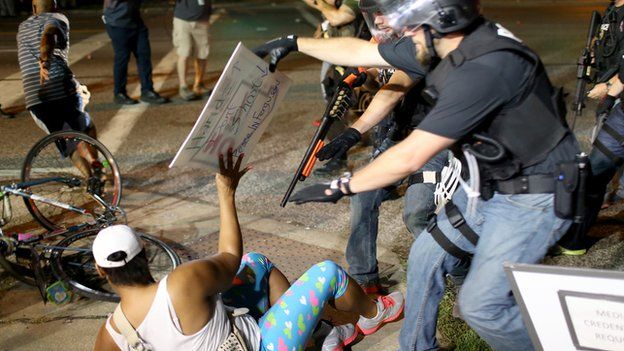 A protestor in Ferguson, Missouri is confronted by a police officer weilding a shotgun.