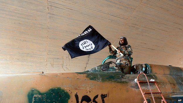 Islamic State fighter waves flag from fighter jet at Tabqa air base. 27 Aug 2014