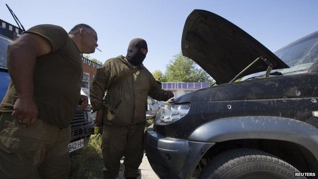 Armed pro-Russian separatists inspect a damaged car in the southern coastal town of Novoazovsk