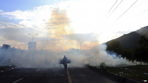 A bicyclist makes his way through tear gas fired by police to disperse protesters