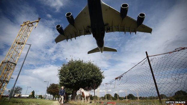 A passenger plane comes into land over a field containing horses at Heathrow Airport