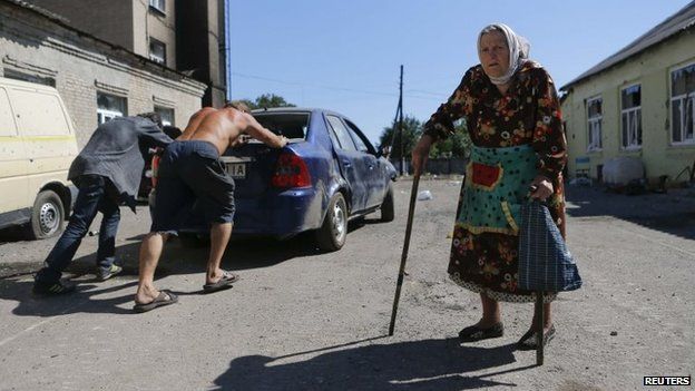People push a broken-down car past a woman in the eastern Ukrainian town of Ilovaysk, 31 August 2014