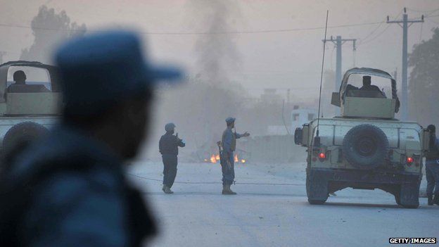 Afghan policemen keep watch as smoke billow in the background after an attack by Taliban militants on the Afghan intelligence service office in Jalalabad on 30 August 2014.