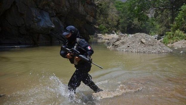 A federal police officer crosses a river on the outskirts of Arteaga during a search for Knights Templar leader Servando Gomez (26 April 2014)