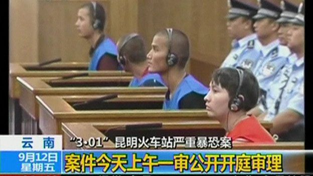 Defendants sit in front of police officers at a courtroom in Kunming City during the trial of four people accused of participating in an attack at a train station in southwestern China, in this still image taken from video on 12 September, 2014