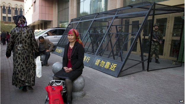 In this 1 May 2014 file photo, a Uighur woman rests near a cage protecting heavily armed Chinese paramilitary policemen on duty in Urumqi in China's northwestern region of Xinjiang