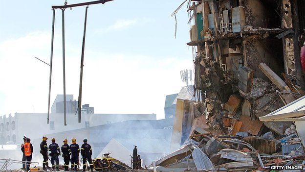 Rescuers stand at the smoking ruins of a building in Christchurch, New Zealand on 24 February, 2011