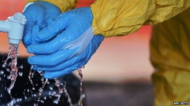 A medical worker in Kailahun, Sierra Leone washes their gloves in chlorine on 15 August 2014.