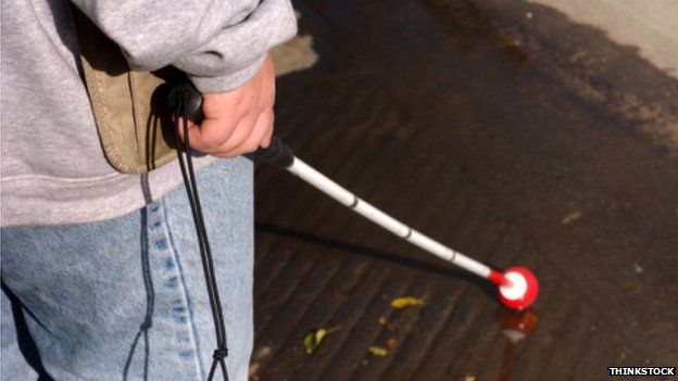 A blind person holding a cane about o cross a road