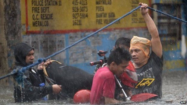 Manila residents hold onto a rope as they wade through floodwater (19 Sept 2014)