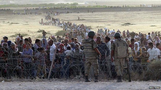 Turkish soldiers stand guard as Syrians wait behind the border fences. 18 Sept 2014
