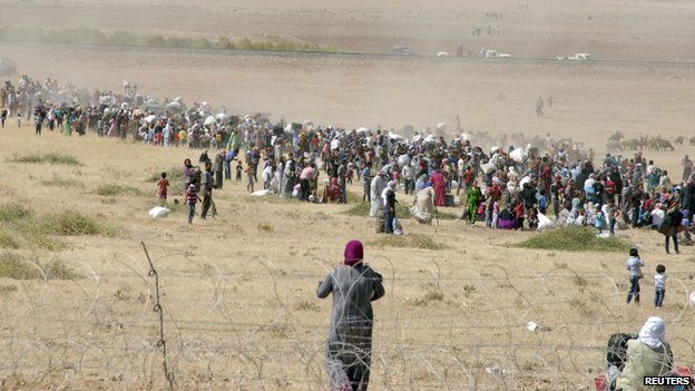 Syrian Kurds wait behind the border fence to cross into Turkey near the south-eastern town of Suruc in Sanliurfa province, 19 September 2014.