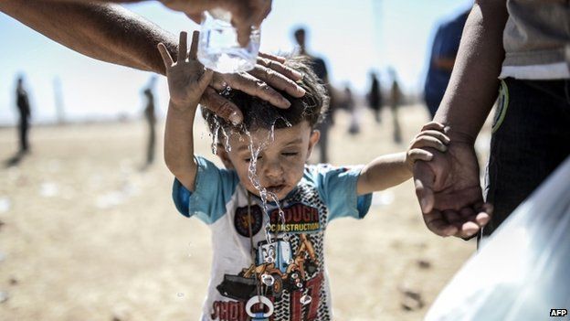 A Syrian Kurd pours water on a child after they crossed the border between Syria and Turkey near the south-eastern town of Suruc in Sanliurfa province, on 20 September 2014.