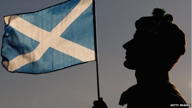 A highlander hold up a Scottish Saltire flag