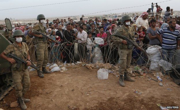 Turkish troops stand guard as Syrian Kurdish refugees wait on the border at Suruc, 27 September