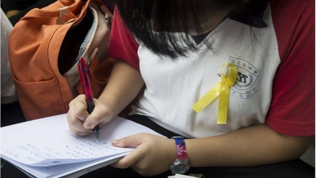 A secondary school student wearing a yellow ribbon attends a lesson conducted by her teacher during a rally outside government headquarters in Hong Kong