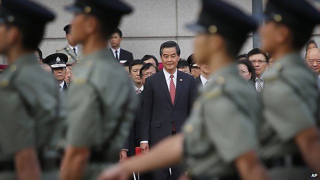 Hong Kong Chief Executive Leung Chun-ying watches as military personnel march during a flag-raising ceremony on Wednesday, 1 October, 2014 in Hong Kong, as thousands of protesters watching from behind police barricades yelled at him to step down