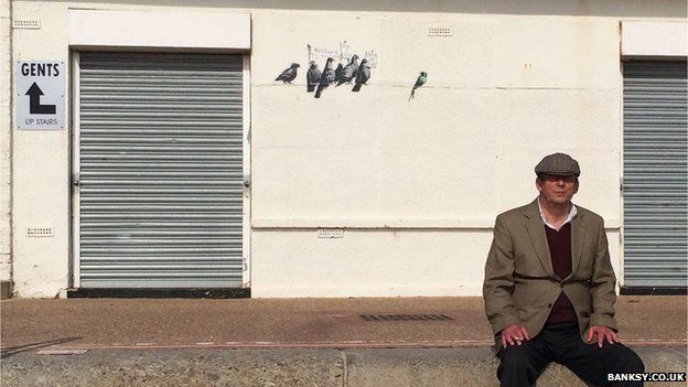 Man sitting in front of Banksy's mural in Clacton