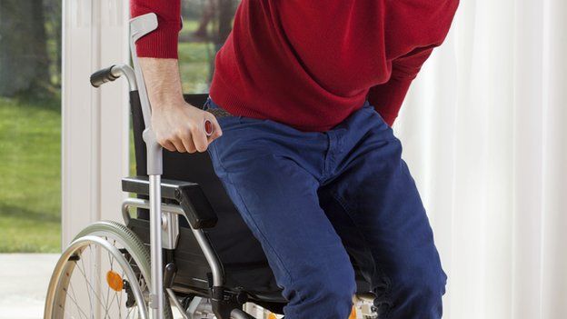 A man using a crutch and getting up out of his wheelchair