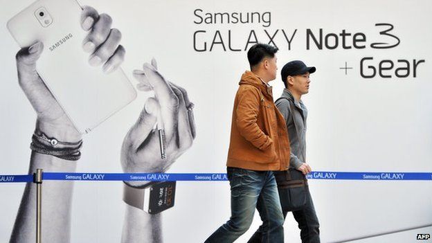 Pedestrians walk past a sign board advertising Samsung Electronics' Galaxy Note 3 smartphone at a railway station in Seoul
