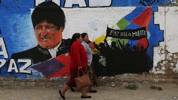 Women walk past a mural featuring Bolivia"s President Evo Morales in La Paz on 10 October 2014