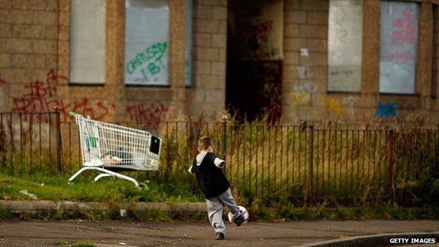 Child playing football in front of boarded up homes in Glasgow