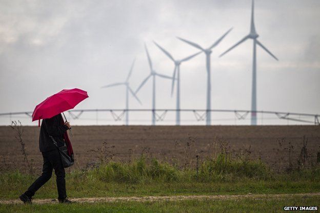 Woman with umbrella walks past wind turbines