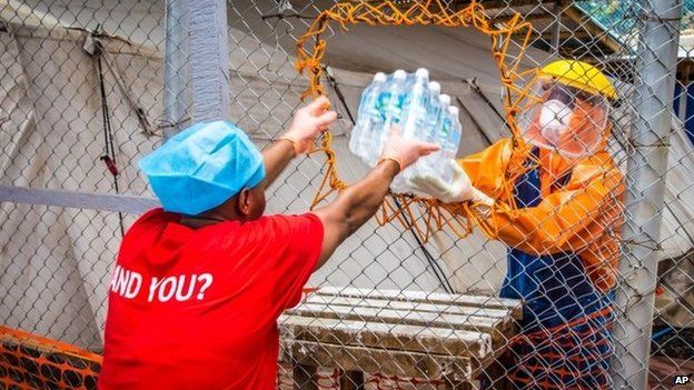 A healthcare worker wearing protective gear hands out water bottles at a treatment centre near Freetown, Sierra Leone, 16 October
