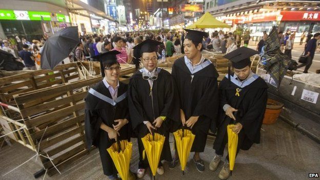 Graduates are seen in their caps, gowns and symbolic yellow democracy umbrellas by barricades in Mong Kok, 19 October 2014