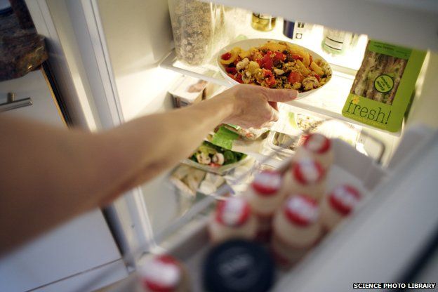 Arm of person putting pasta dish in fridge