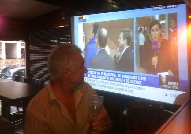 A man in a bar with BFMTV on the television screen in the background