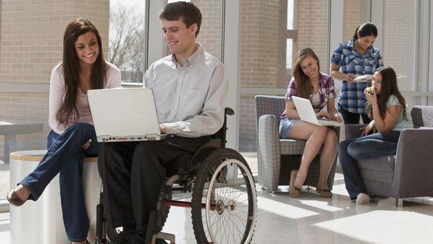A man in a wheelchair looking at his laptop with a woman sitting next to him.