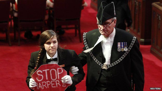 Senate page Brigette DePape, holding a sign reading "Stop Harper" is led from the room by Sergeant-at-Arms Kevin Vickers (R) in the Senate chamber on Parliament Hill in Ottawa in this file photo from June 3, 2011.