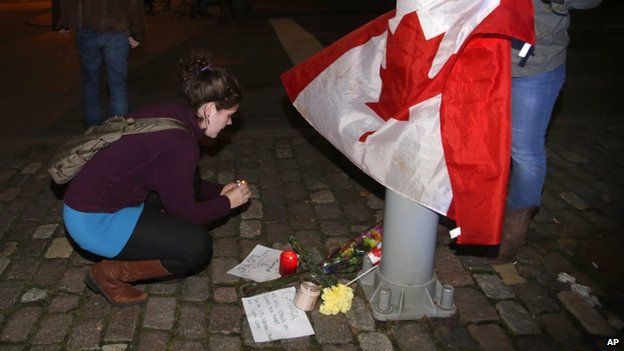 Mourners light a candle and tie a Canadian flag around a light pole near the National War Memorial after a soldier was killed in Ottawa on Wednesday, Oct. 22, 2014