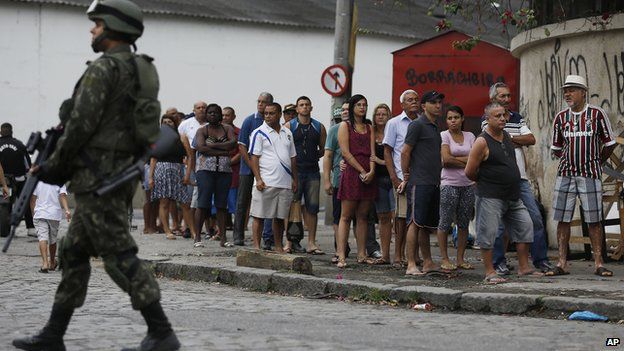 A soldier patrols where people wait in line to vote in general elections outside a school at the Mare Complex slum in Rio de Janeiro, Brazil, Sunday, Oct. 26, 2014