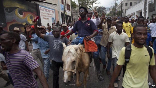 Senator Moise Jean Charles, riding second on the horse, participates in a anti-government protest in Port-au-Prince on 26 October, 2014