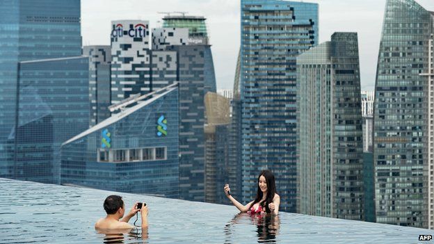 A couple take their photo from the Marina Bay Sands swimming pool overlooking Singapore's business district