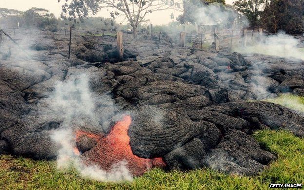 Lava flow burns through thick vegetation and a fence