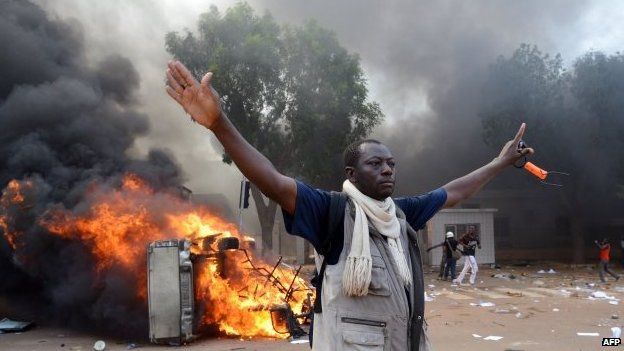 A man stands in front of a burning car, near the Burkina Faso's Parliament where demonstrators set fire to parked cars - 30 October 2014, Ouagadougou, Burkina Faso
