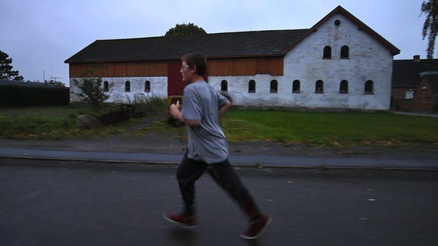 Mike running along a road with rural building in the background