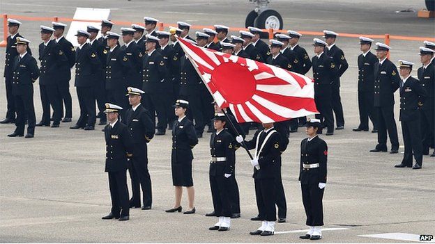 Navy servicemen of the Japan Self-Defense Force stand with their flag prior to a review ceremony on a runway at the Japan Air Self-Defense Force's Hyakuri air base in Omitama, Ibaraki prefecture on 26 October 2014.