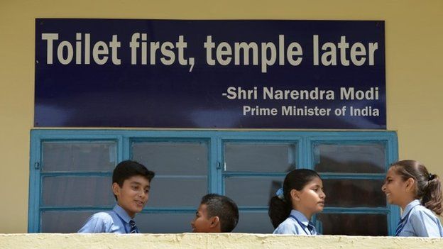 In this September 22, 2014, photo schoolchildren talk in front of a poster bearing a quote from PM Narendra Modi in Delhi.