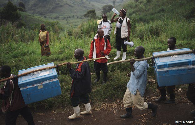 Porters carry accumulators filled with ice to keep live vaccines cold